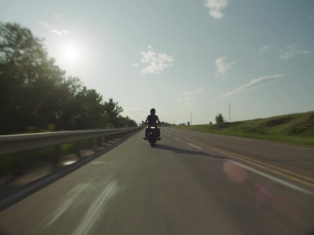 An adult rides a motorcycle on a rural highway on a mostly sunny day