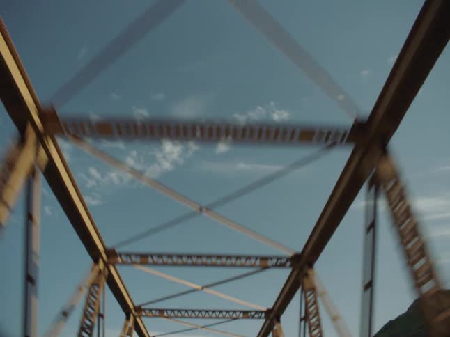 The bridge has crossing steel beams at the top