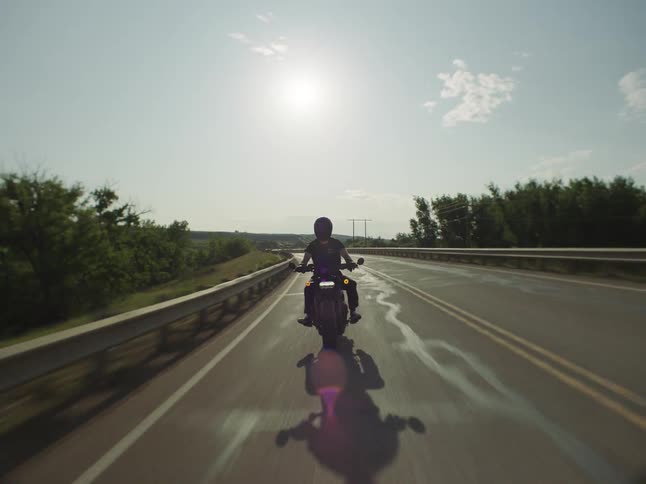 Motorcyclist rides along a wet road under the intense afternoon sun