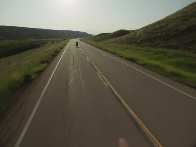 Motorcyclist rides alone on a deserted road surrounded by green hills