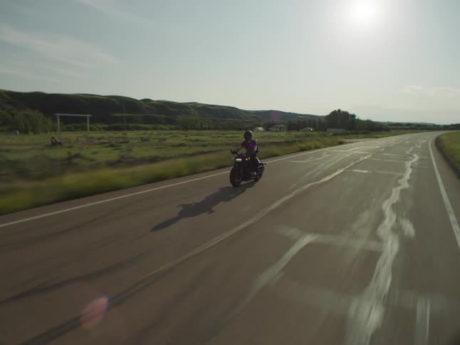 The man is riding his motorcycle past the green grass