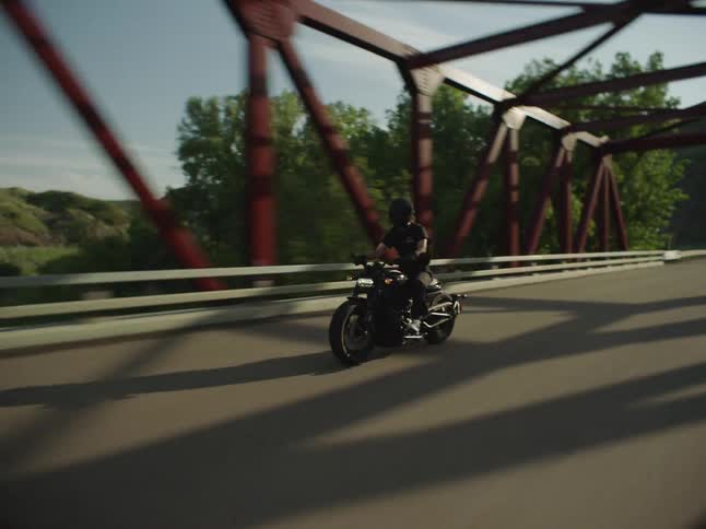 Motorcyclist rounds a curve on a road surrounded by hills at dusk