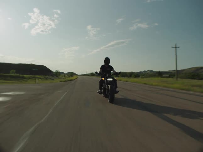 An adult rides a motorcycle on a rural highway on a mostly sunny day
