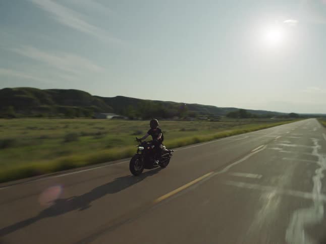 Motorcyclist travels along a road passing the hills in the rural countryside on a slightly cloudy day