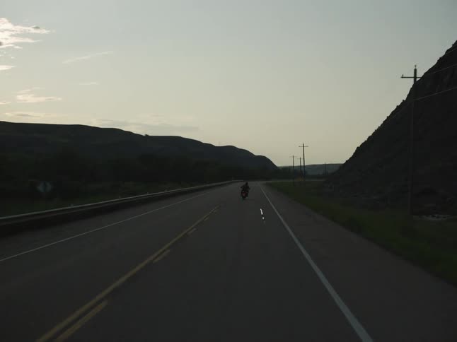 Motorcyclist travels along a highway passing multiple hills at dusk