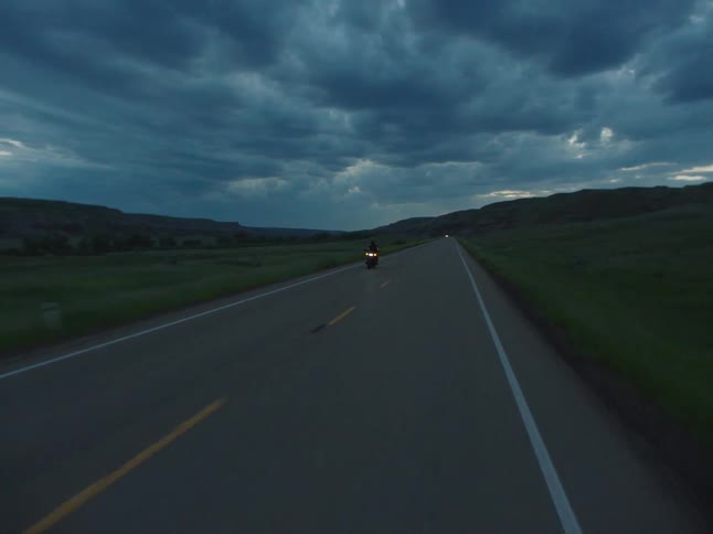 Motorcyclist rides along a deserted road under a cloudy sky at dusk