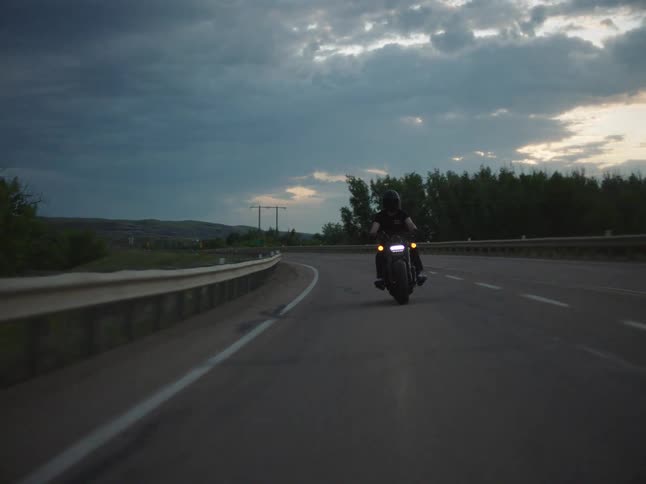 Motorcyclist takes a curve on a road surrounded by trees at dusk