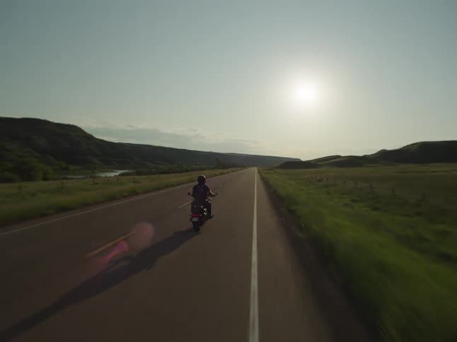 The motorcycle rides down the road surrounded by greenery