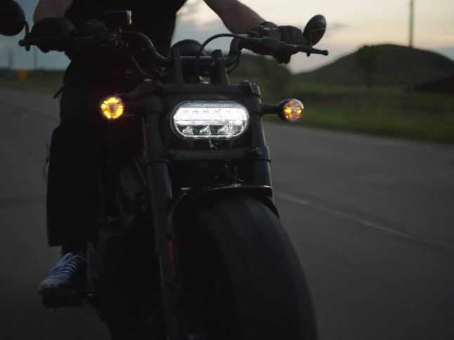 Motorcyclist rides toward the horizon with headlights on at dusk