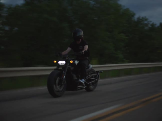 Motorcyclist rides along a road at dusk under a cloudy sky