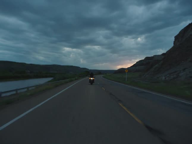 Motorcyclist rides along a deserted road under a cloudy sky at dusk