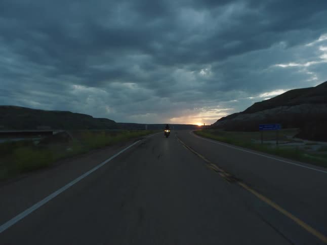 A person rides a motorcycle on a countryside highway at sunset