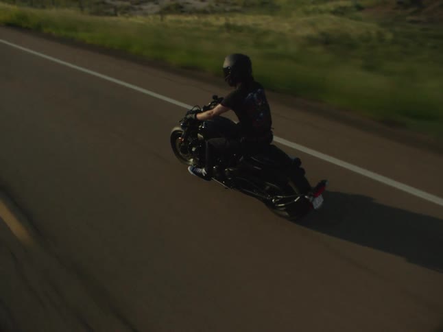 A person riding a motorcycle on a rural road across a grassy land with many hills