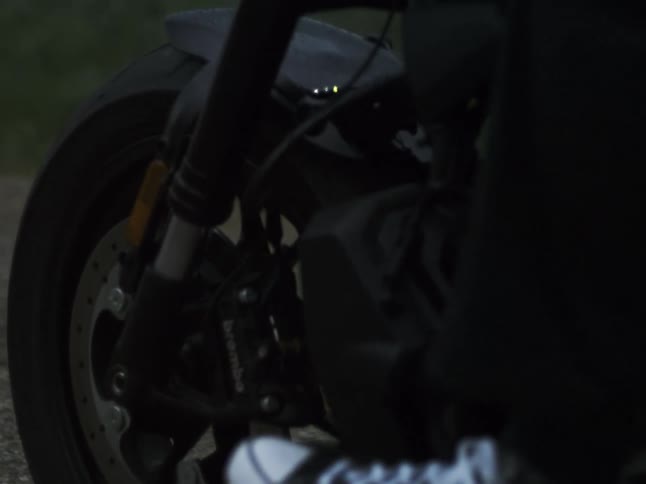 A motorcycles wheels spin as a person rides it down the road at midday