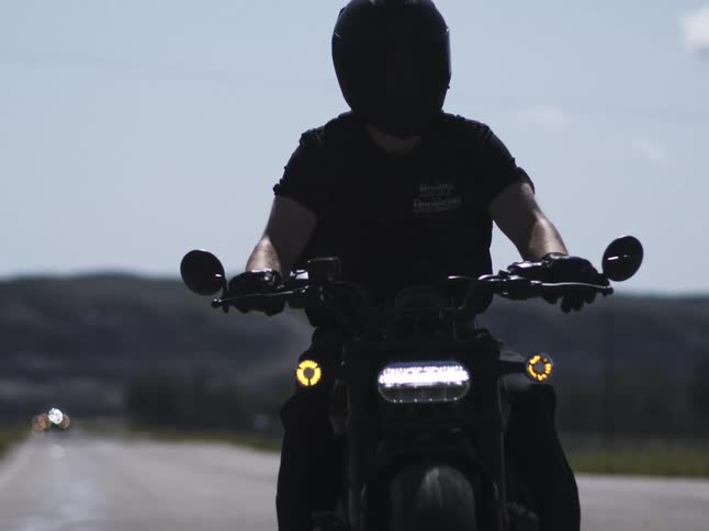 Motorcyclist rides along the road with lights on under a clear sky
