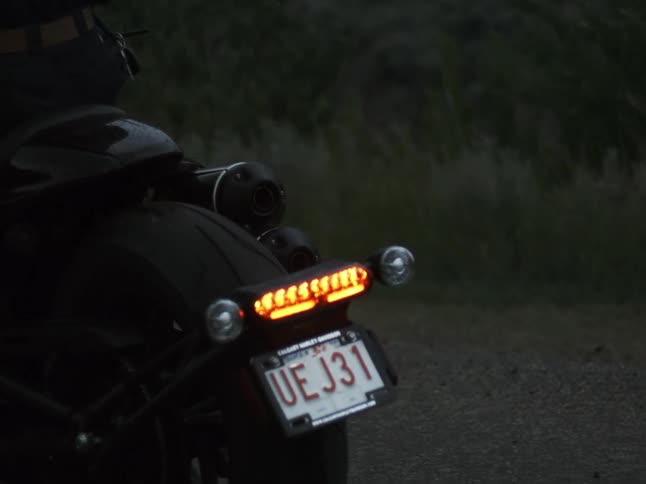 Rear light on and visible license plate of a motorcycle stopped on the roadside