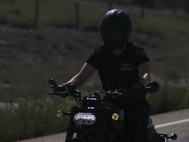 A man riding a motorcycle on a country road with his t shirt flapping in the wind