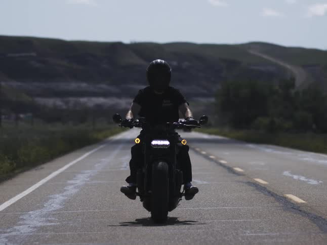 The man is riding away from the mountains on his motorcycle