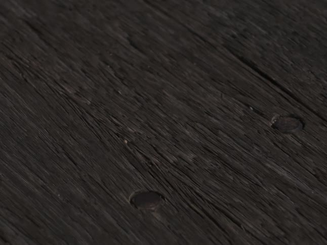 A slow tracking shot glides across weathered dark wooden planks highlighting deep grain cracks and scattered round rivets in soft light