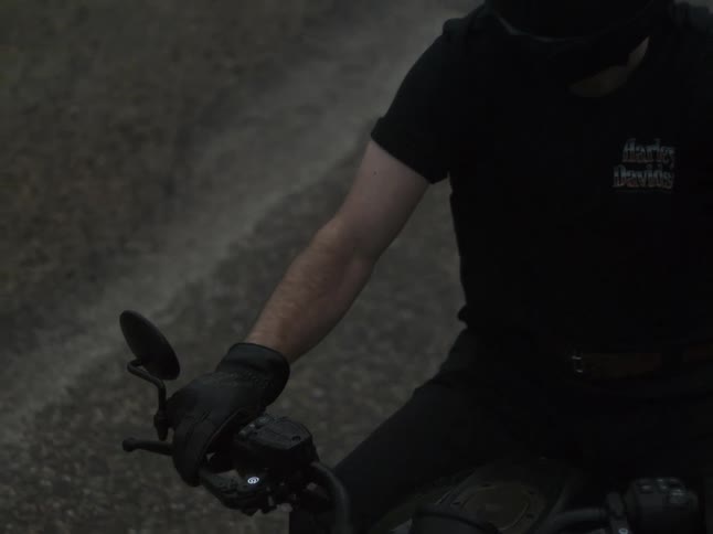Person rides motorcycle with headlight on and turn signal flashing over dark wet asphalt