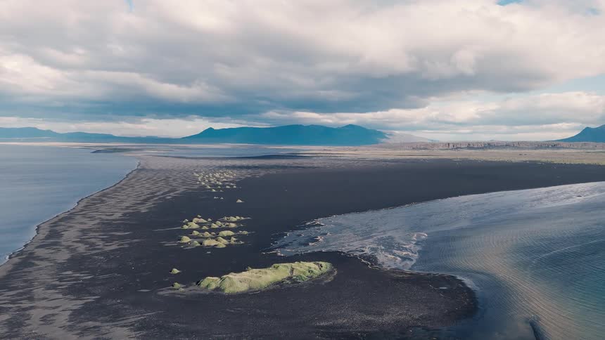 Dark peninsula extending over blue waters under a cloudy sky