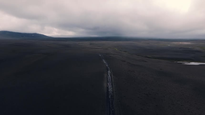 Narrow river cutting through a vast dark landscape under a cloudy sky