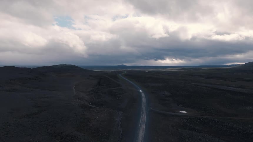 Lonely road crossing dark terrain under a heavy clouded sky