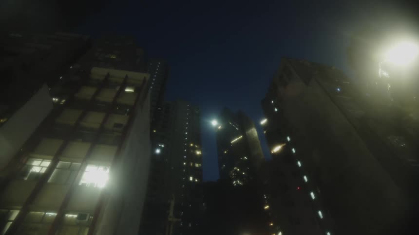 A verticallyoriented view of multiple structures with illuminated windows and a prominent bright light source on a dark background