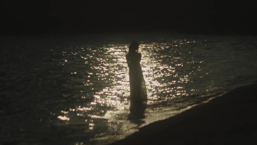 Silhouette of a woman walks along the seashore illuminated by the sunset reflection