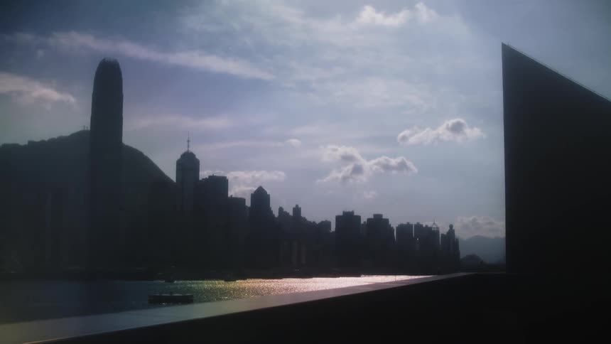 Waterside city skyline stands silhouetted against a cloudy blue sky