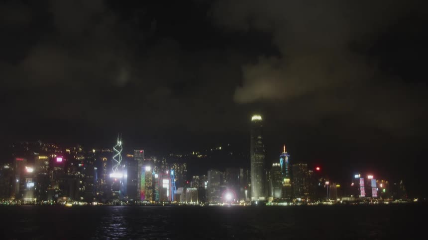 A vibrant city skyline illuminates the night with tall buildings and a ferris wheel reflected in the dark water below