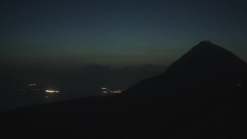 Silhouetted mountain with faint city lights and ocean below at night