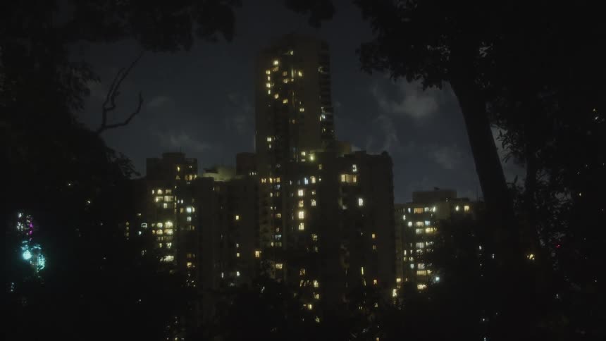 A tall apartment building surrounded by trees illuminated at night