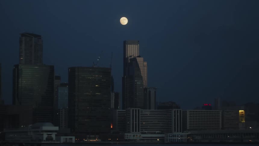 A city skyline with a dark blue sky overhead and a full moon