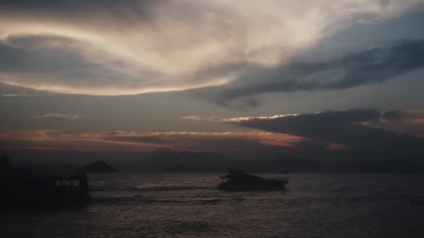 Boats silhouetted against dramatic clouds over the ocean at sunset