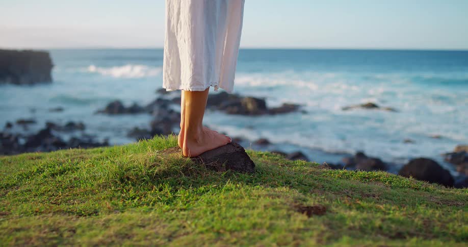 Bare feet on the grass by the sea at sunset