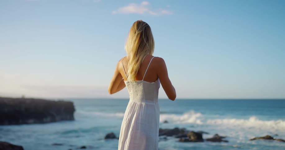 Woman looks at the sea horizon with her hand on her forehead under a clear sunny sky
