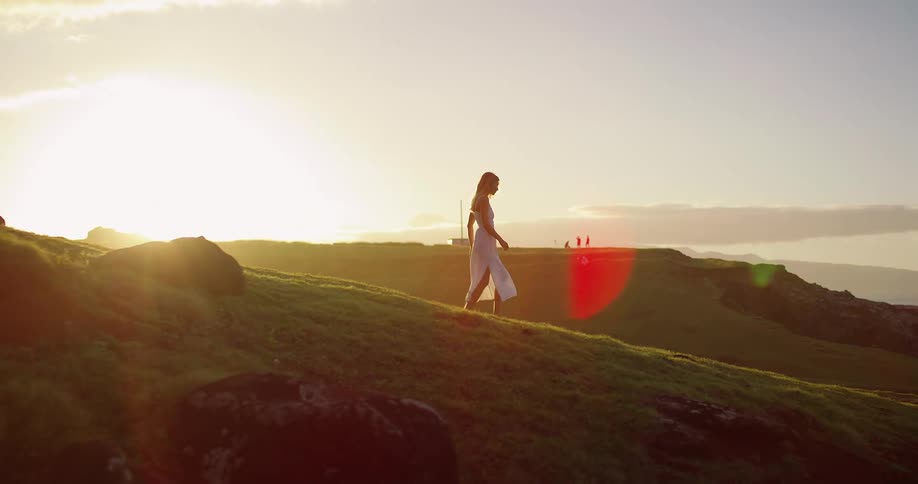 Woman walking on grassy hill during sunset