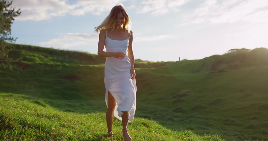 Happy woman in a white dress running down grassy hillside on a summer day