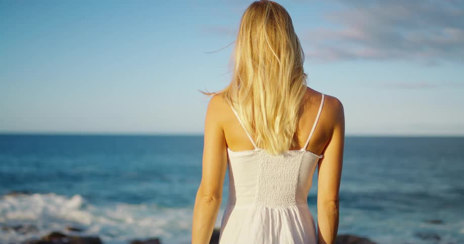 Woman in a white dress gazes at the sea under the clear blue sky