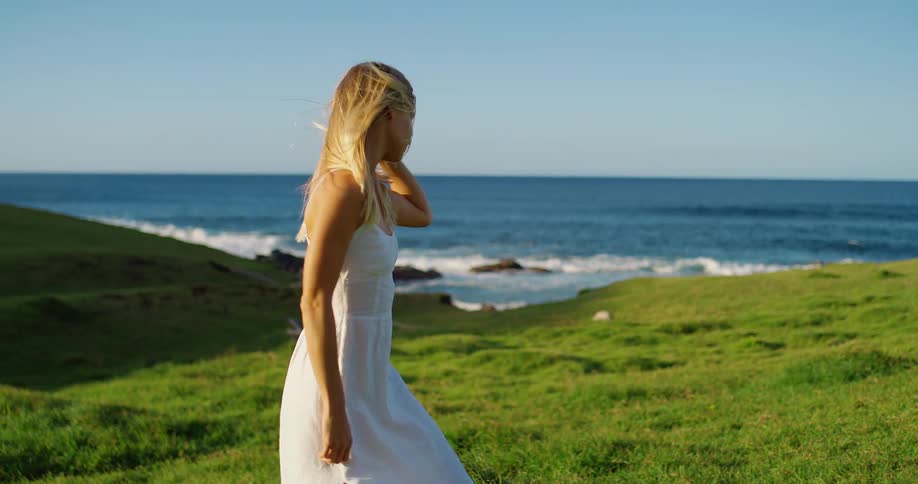 Woman in white dress on grassy field by the sea under blue sky