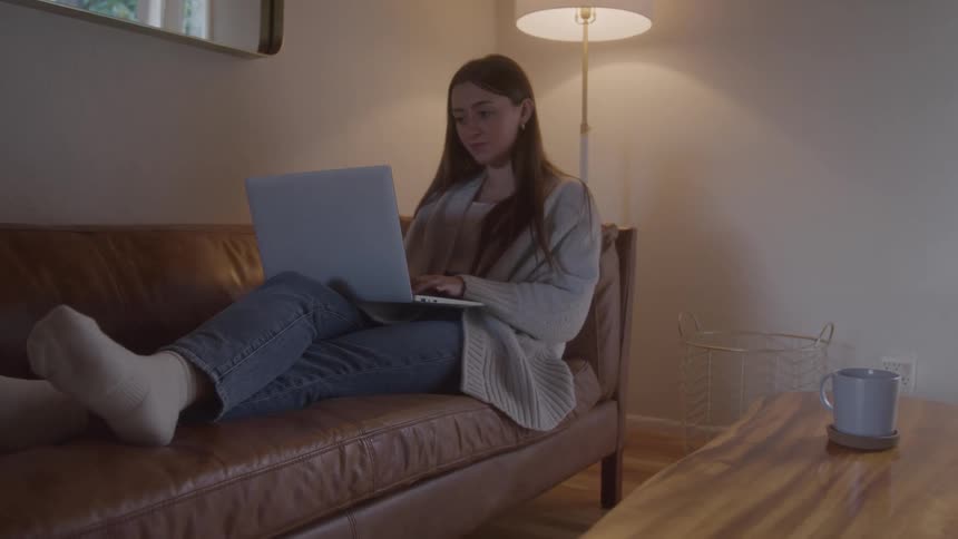 Woman sitting on the sofa works on a laptop in a cozy setting