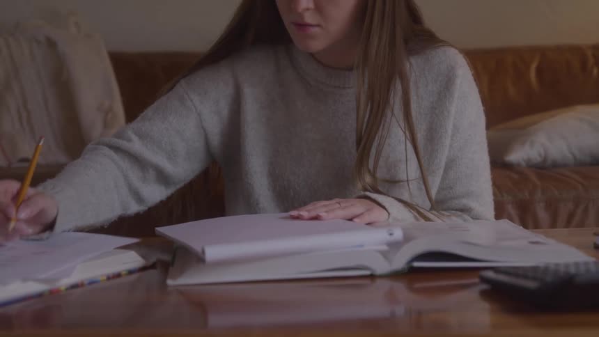 A woman in a living room is sitting and writing on a note pad