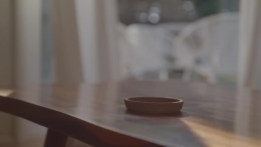 A womans hand places a mug on a holder on the living room table at midday