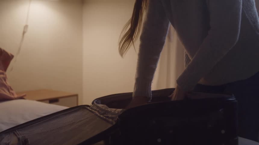 A woman is packing clothes into an open suitcase in a bedroom