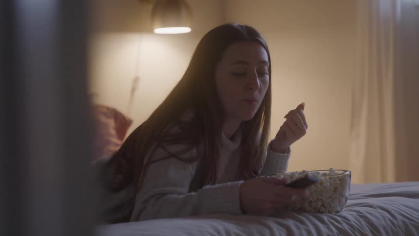 Woman eating popcorn while using a remote control