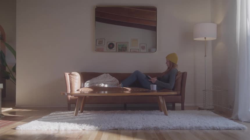 The woman walks into the living room with coffee and her laptop