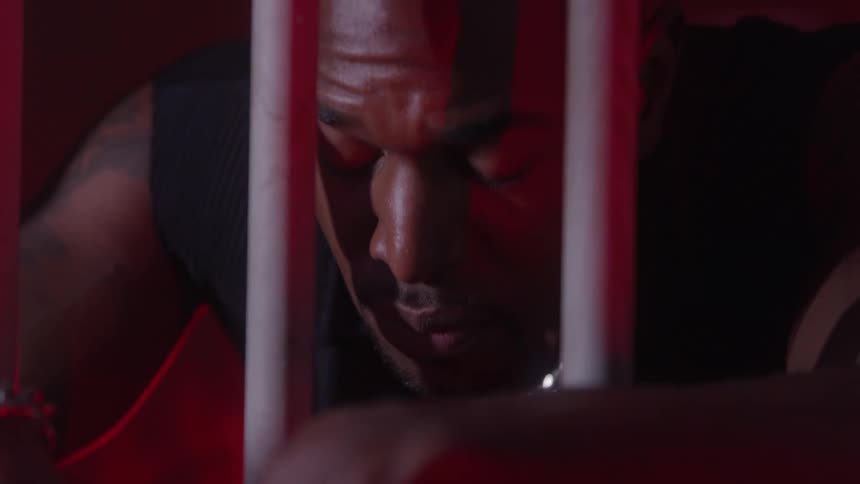 Man leaning behind bars in room with red lighting