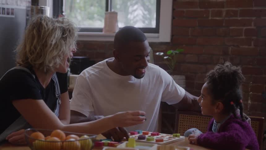 Father and mother teaching their daughter about alphabets with a game while sitting at a table indoors during daytime