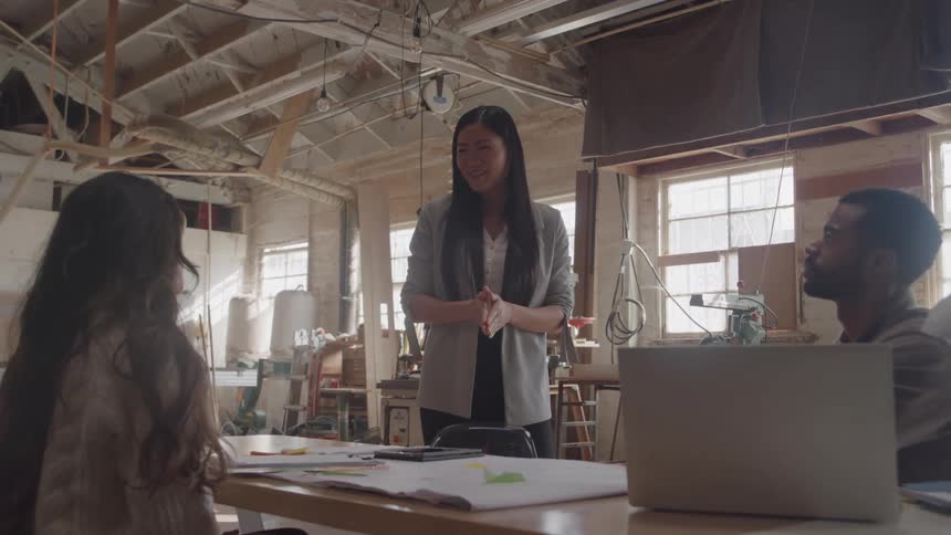Group of three people engages in collaborative discussion in studio with natural light and work materials on the table